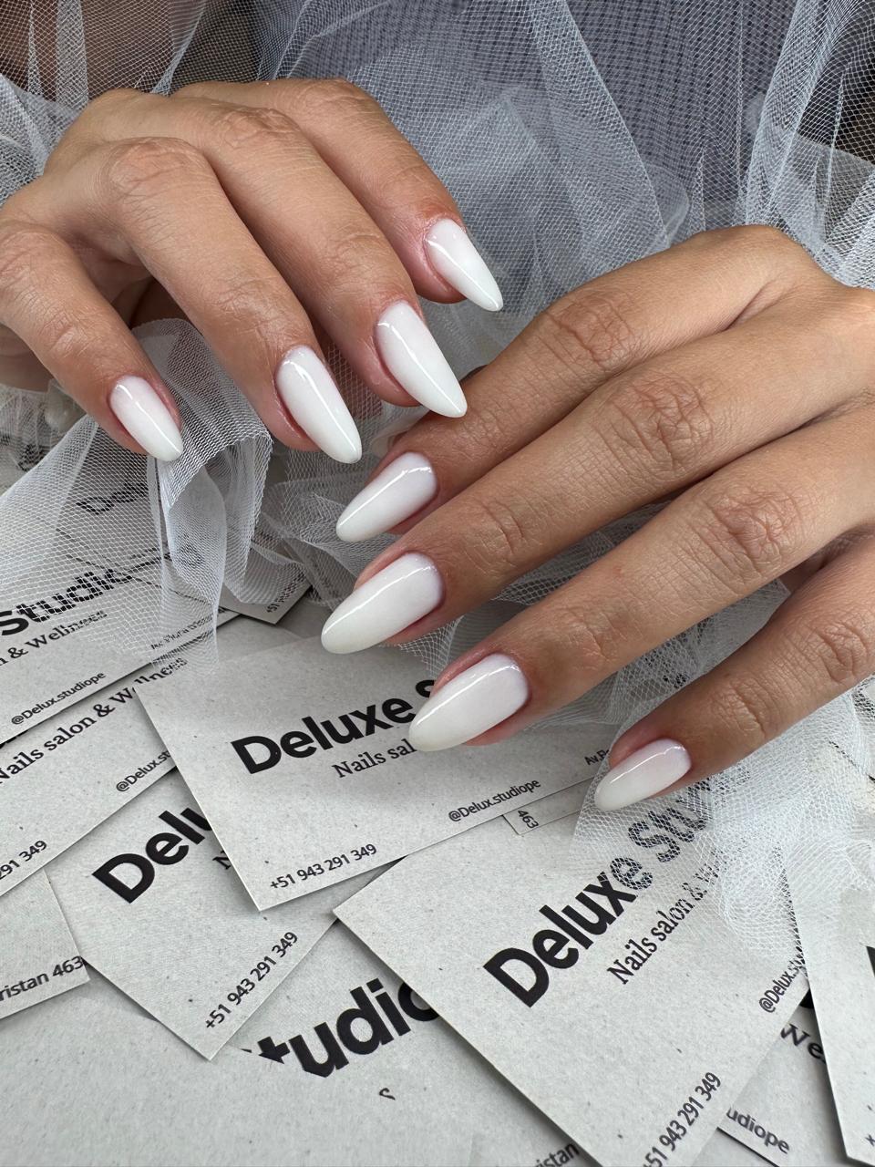 Uñas almendradas en blanco perlado sobre un velo de tul
