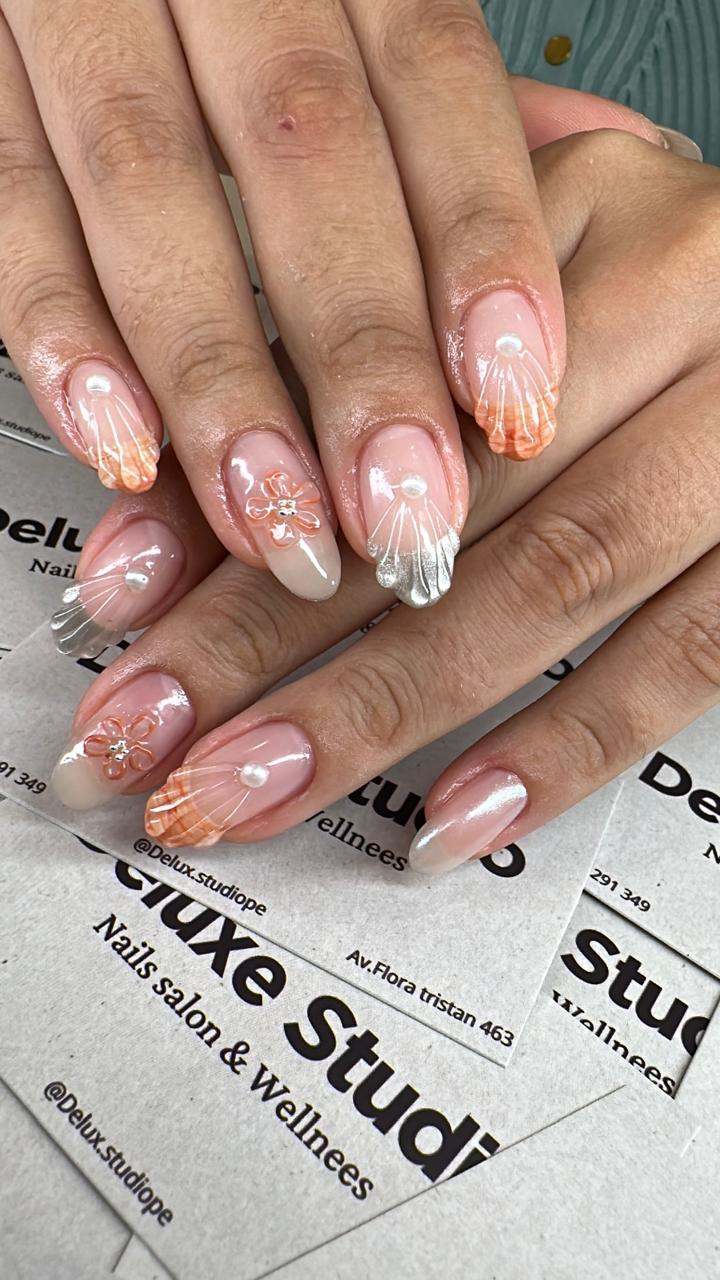Uñas en tono durazno con flores, perlas y detalle plateado