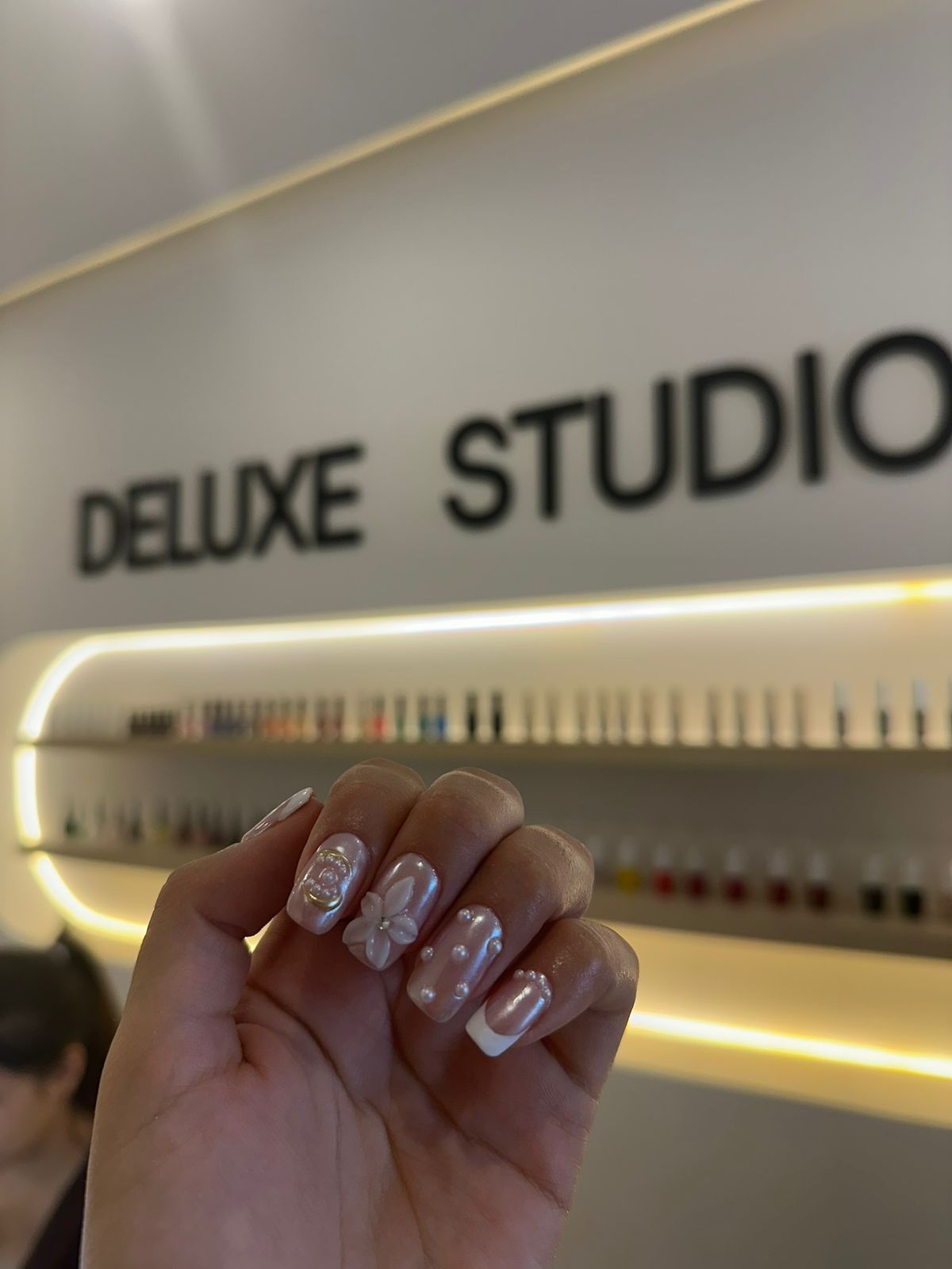 Uñas nacaradas con una flor en relieve y perlas, bajo el rótulo del salón