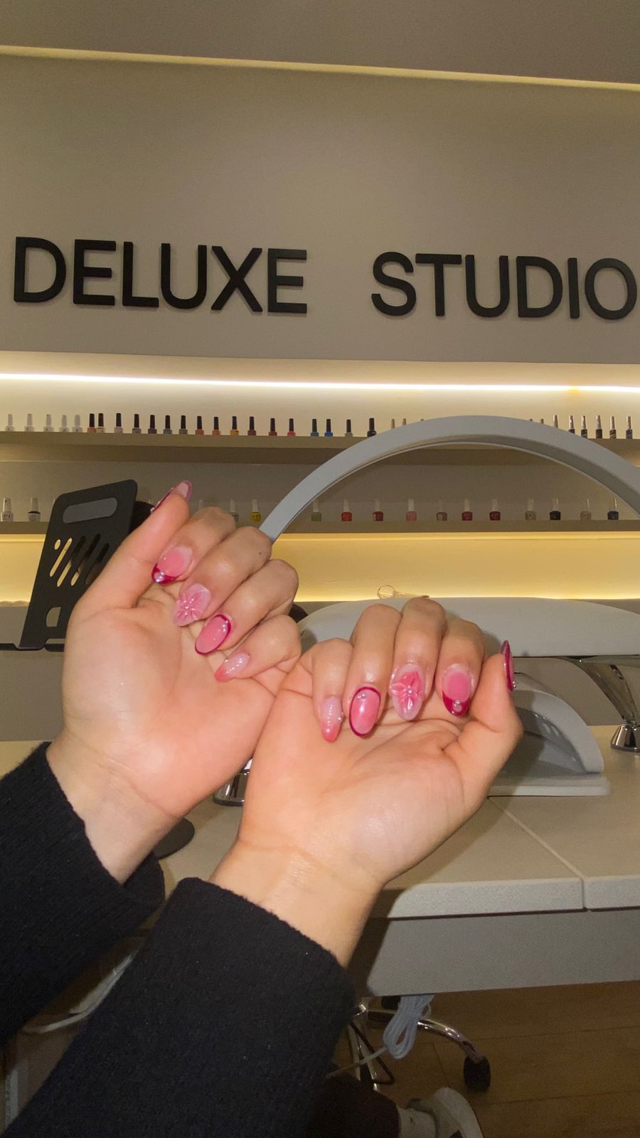 Uñas almendradas en rosa con flores en relieve, bajo el rótulo del salón